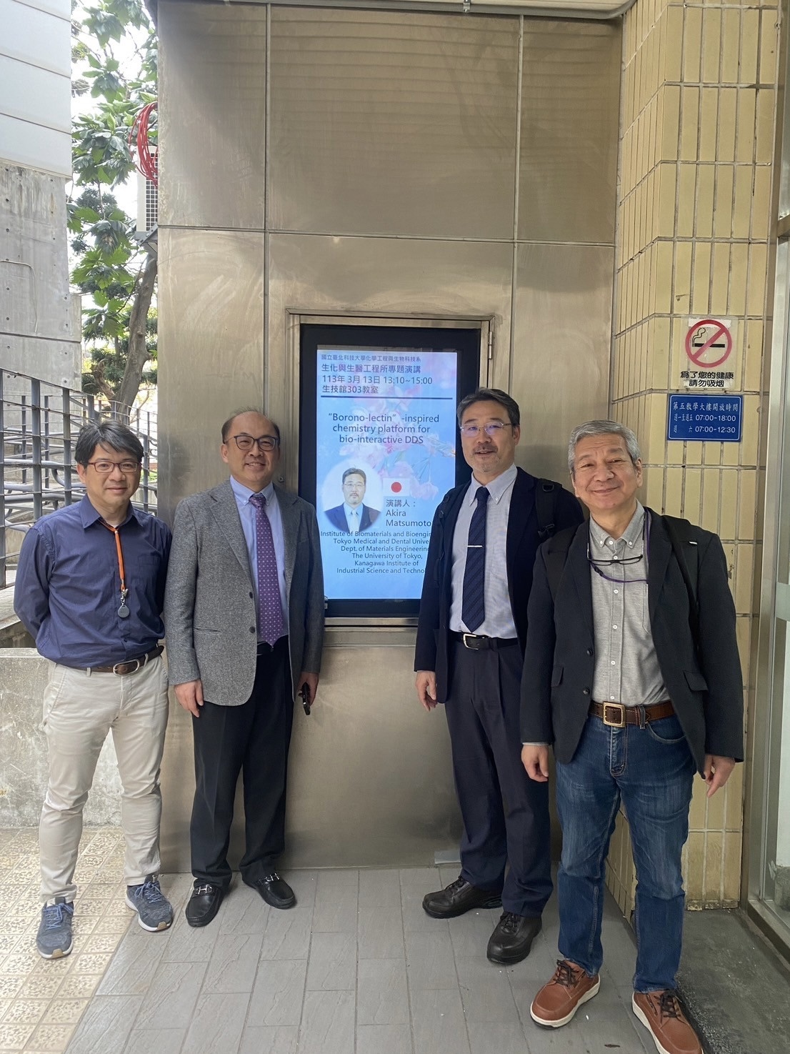The professors pose for a group photo in front of Professor Akira Matsumoto's electronic poster display.