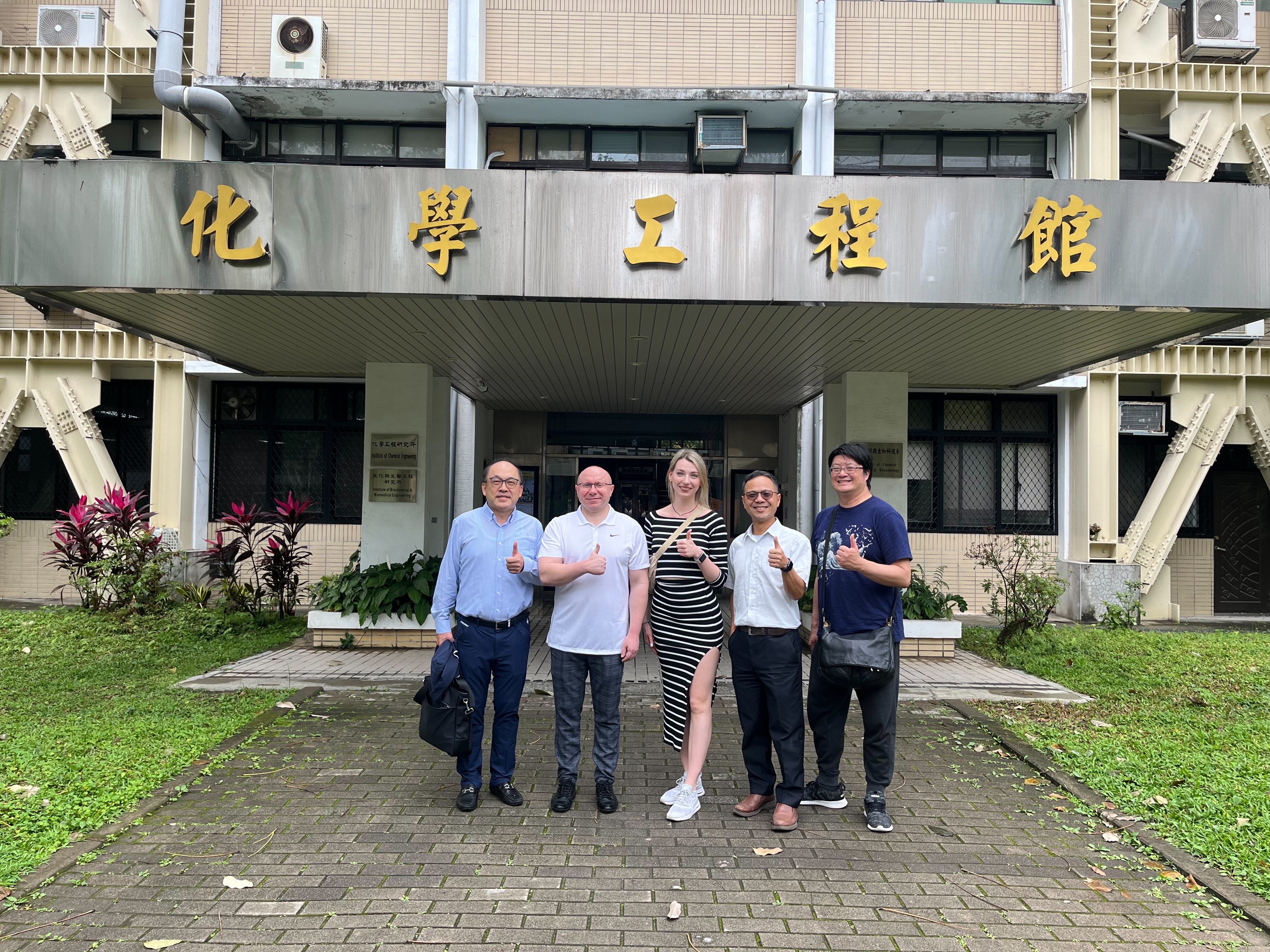 Professors from Gdańsk University of Technology and National Taipei University of Technology pose with thumbs up in front of the Department of Chemical Engineering Building at National Taipei University of Technology.