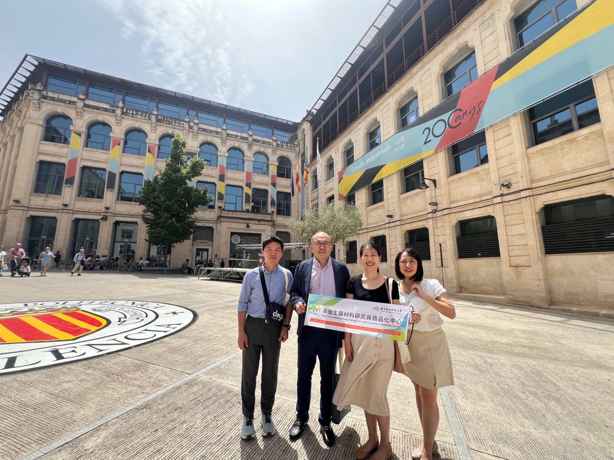 The Center members participating in the visit pose for a group photo while holding the Center's banner in the plaza outside the venue.