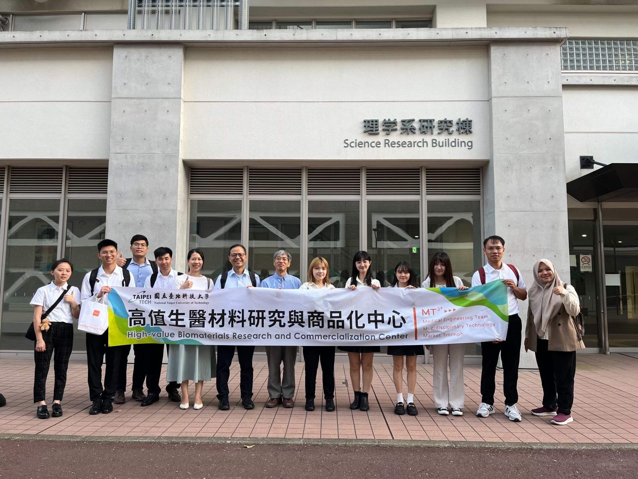 The professor and students pose for a group photo with a banner outside the conference venue